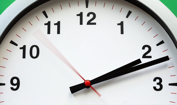 A black and white clock where the seconds hand is moving very quickly on a green background.