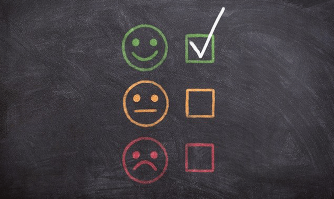 A blackboard with green yellow and red smiley faces drawn on it in chalk. The green face is ticked to suggest a positive experience. 