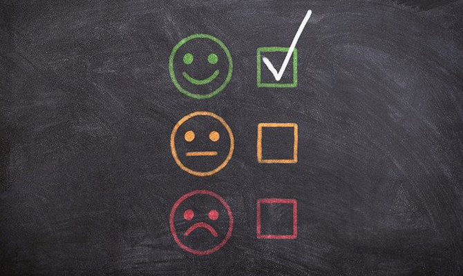 A blackboard with three smiley faces, a green orange and red face and there's a tick next to the green face.